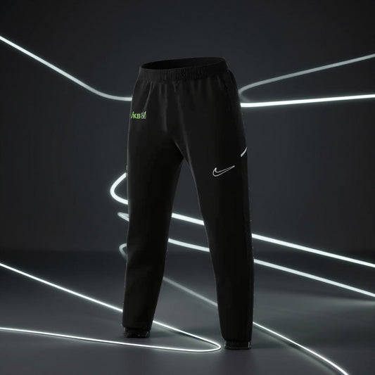 Schwarze Nike Dri-FIT Academy Woven Soccer Track Pants mit weißem Swoosh-Logo und grünem VKB-Logo vor dunklem Hintergrund mit leuchtenden Linien.